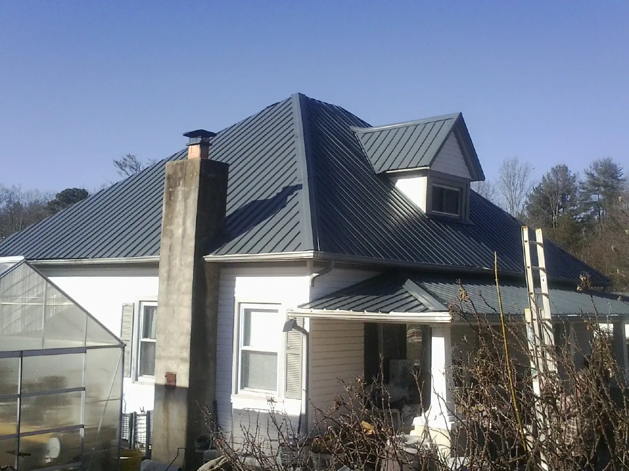 Dark blue standing seam metal roof on a white farmhouse with dormer — Slate & Tile Roof Repair by Roofing Brothers in Bay Village
