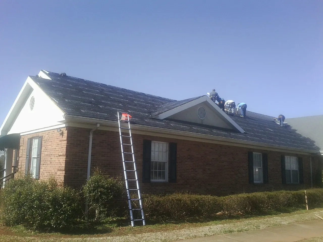 Crew tearing shingles off a brick ranch roof with a ladder set — Metal Roof Repair work by our crew in Bay Village