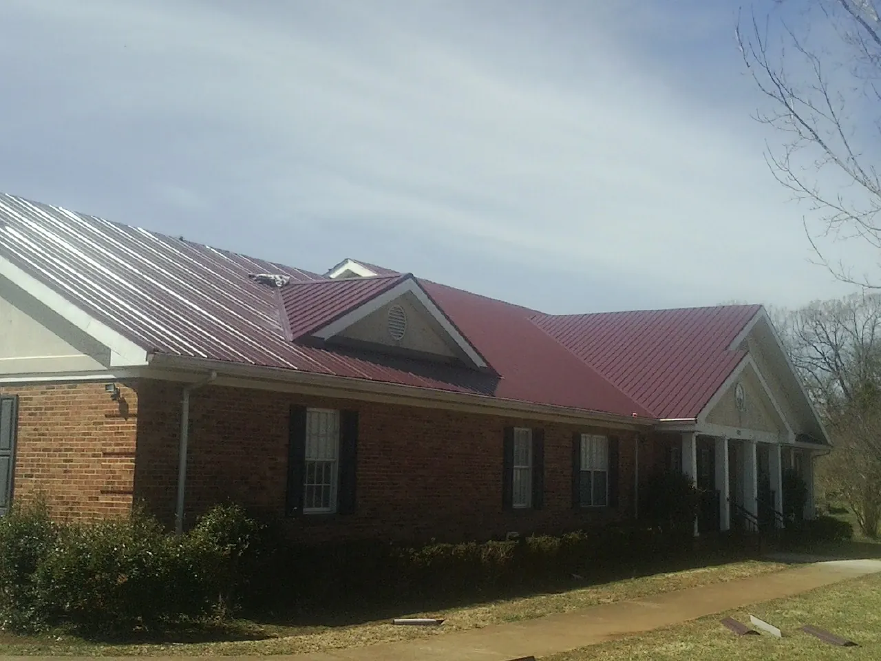 Red metal roof with gabled entries on a long brick building, from a Hail Damage Roof Repair job in Bay Village