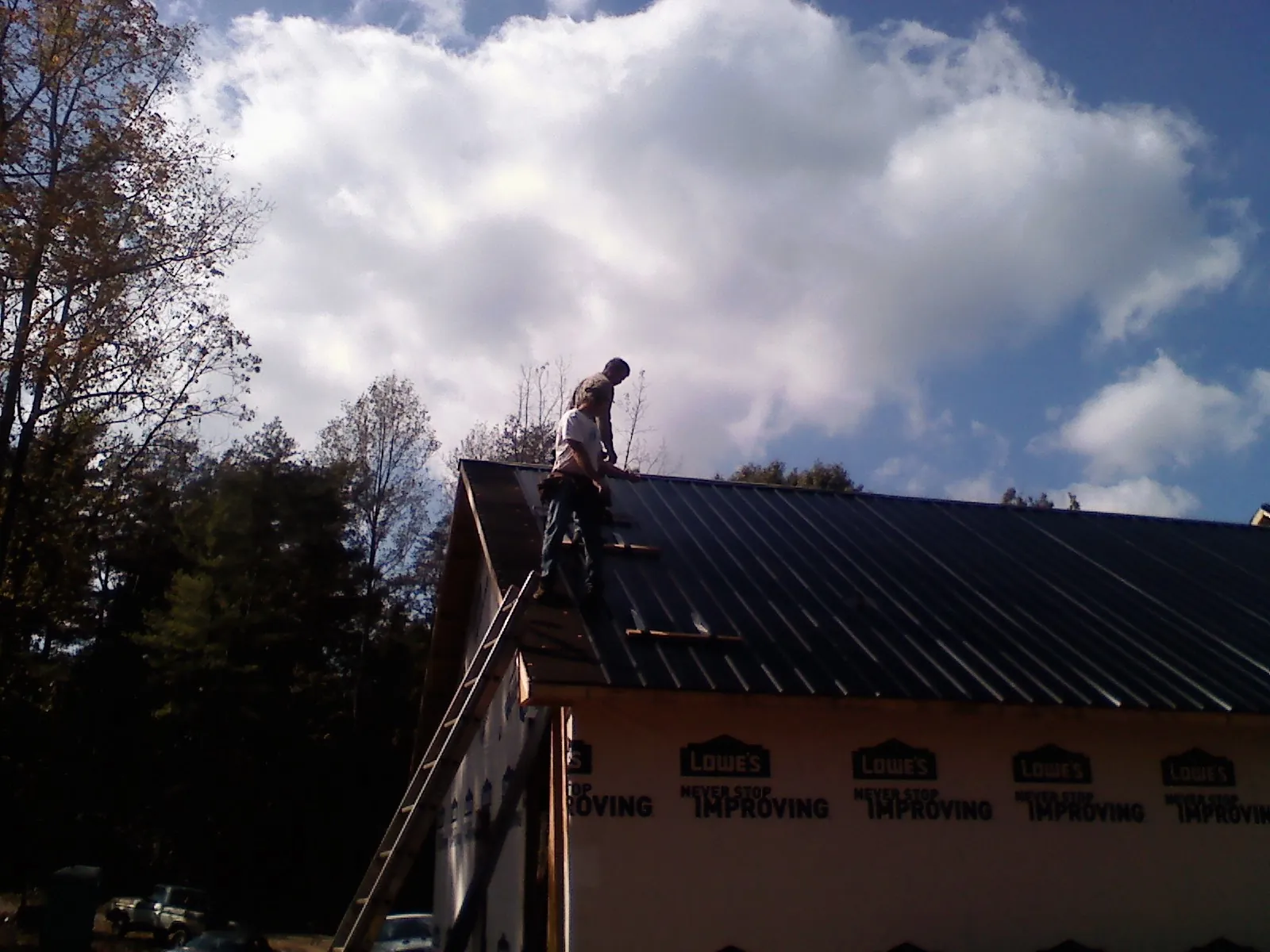 Roofer fastening dark metal panels high against a cloudy sky, from a Roof Inspection job in Bay Village
