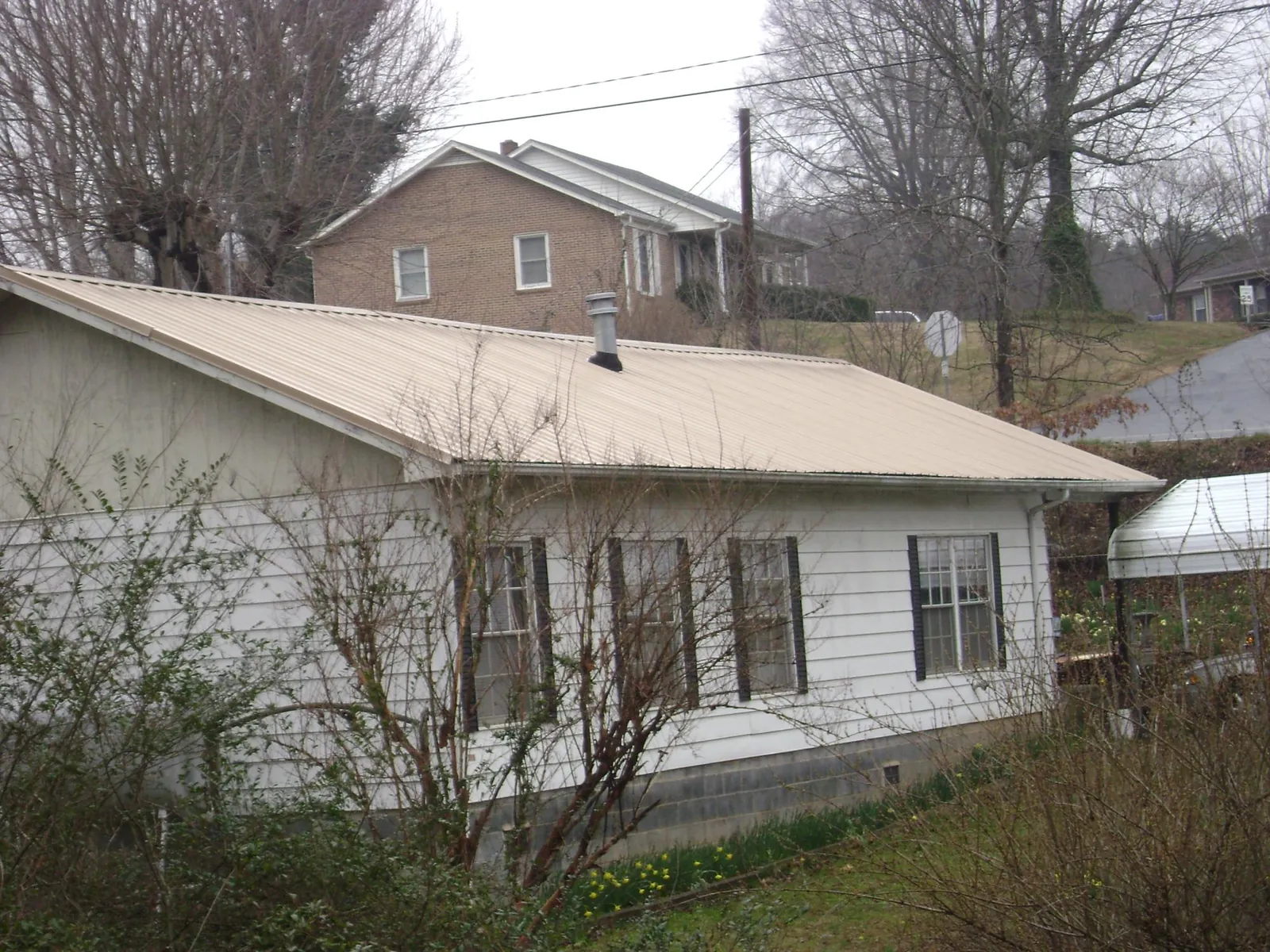 Tan metal roof on a white sided house set into a hillside — Commercial Roofing by Roofing Brothers in Bay Village